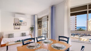 A dining area with a table set for four, a sofa with a 'HOME' sign, and a view of the street and buildings. - Colmeia AL - Casa Néctar (Armação de Pêra)