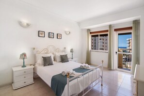 Een hotelkamer met een bed, nachtkastjes, uitzicht op zee en een balkon.
