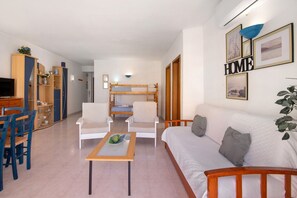 Een woonkamer met een bank, stoelen, een salontafel, een televisie en een stapelbed op de achtergrond.