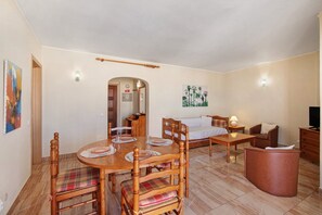 Un comedor con mesa y sillas de madera, un sofá, un mueble para televisión y una lámpara.