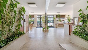 A spacious lobby with a high ceiling, large windows, and potted plants. - Colmeia AL - Casa Mel: Vista Mar e Conforto em Armação de Pera (Unknown)
