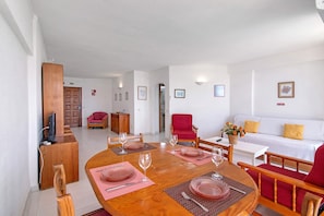 Un comedor con una mesa de madera dispuesta para cuatro personas, rodeada de sillas rojas, un sofá blanco y un sillón rojo.