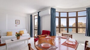 A dining area with a table set for four, a sofa, and a window with a city view. - Colmeia AL - Casa Mel: Vista Mar e Conforto em Armação de Pera (Unknown)