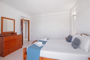 Una habitación de hotel con un aparador de madera, una cama con ropa blanca y un espejo sobre el aparador.