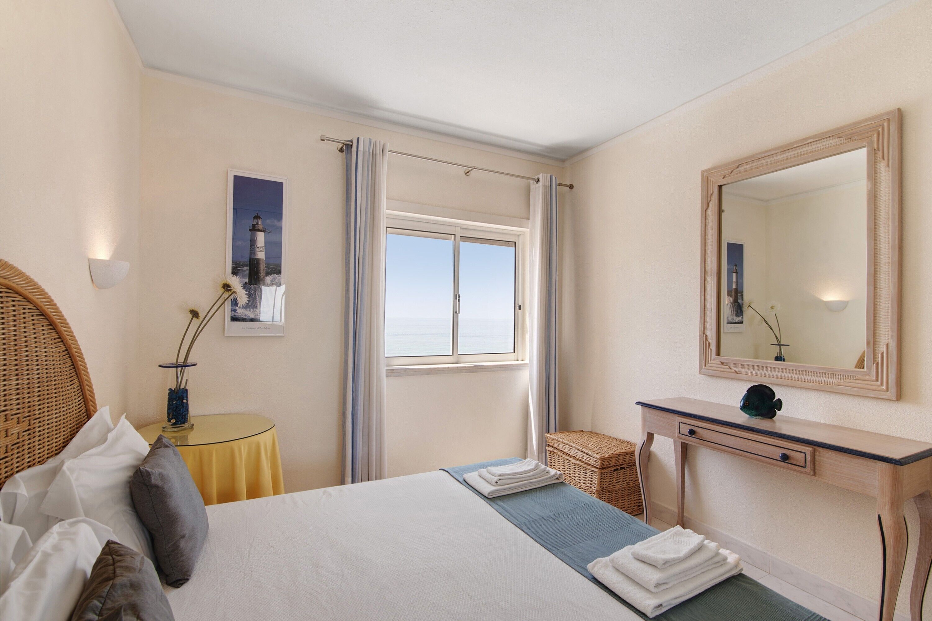 Una camera da letto con un letto, un comodino, uno specchio, una finestra con tende e un quadro appeso al muro.