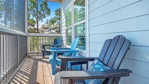 A covered porch with blue Adirondack chairs and a table, overlooking a forested area. - 4 Bedroom Pet Friendly House in Fort Morgan - Free Daily Activities! (Gulf Shores)