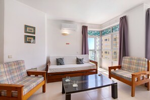 Una sala de estar con un sofá, dos sillones, una mesa de centro y una ventana con cortinas.