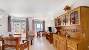Een woonkamer met een bank, een eettafel, stoelen, een televisie en houten kasten.