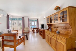 Una sala de estar con sofá, una mesa de comedor, sillas, un televisor y armarios de madera.