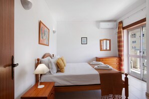 A bedroom with a bed, bedside table, lamp, and a window with curtains. - Colmeia AL - Casa Cera: Apartamento com Vista Mar em Armação de Pera (Armação de Pêra)