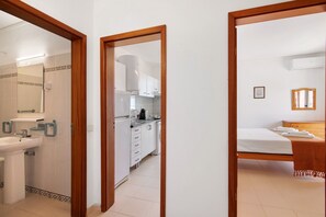 A bathroom with a sink and mirror, a kitchen with cabinets and appliances, and a bedroom with a bed and dresser. - Colmeia AL - Casa Cera: Apartamento com Vista Mar em Armação de Pera (Armação de Pêra)