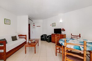 A living room with a sofa, a dining table with chairs, a television, and a cabinet. - Colmeia AL - Casa Ferrão (Armação de Pêra)