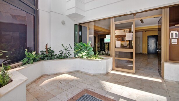 Un vestíbulo moderno con piso de baldosas, un mostrador de recepción y una puerta de cristal que da a un pasillo.