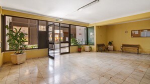 Un espacio interior amplio con suelo de baldosas, un banco, plantas en macetas y una puerta de cristal que da al exterior.