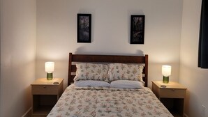 Une chambre à coucher avec un lit en bois, deux lampes de chevet, un ventilateur de plafond et deux tableaux encadrés accrochés au mur.