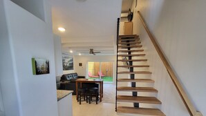 Un escalier avec des marches en bois et une rampe, menant à un coin repas équipé d’une table et de chaises.