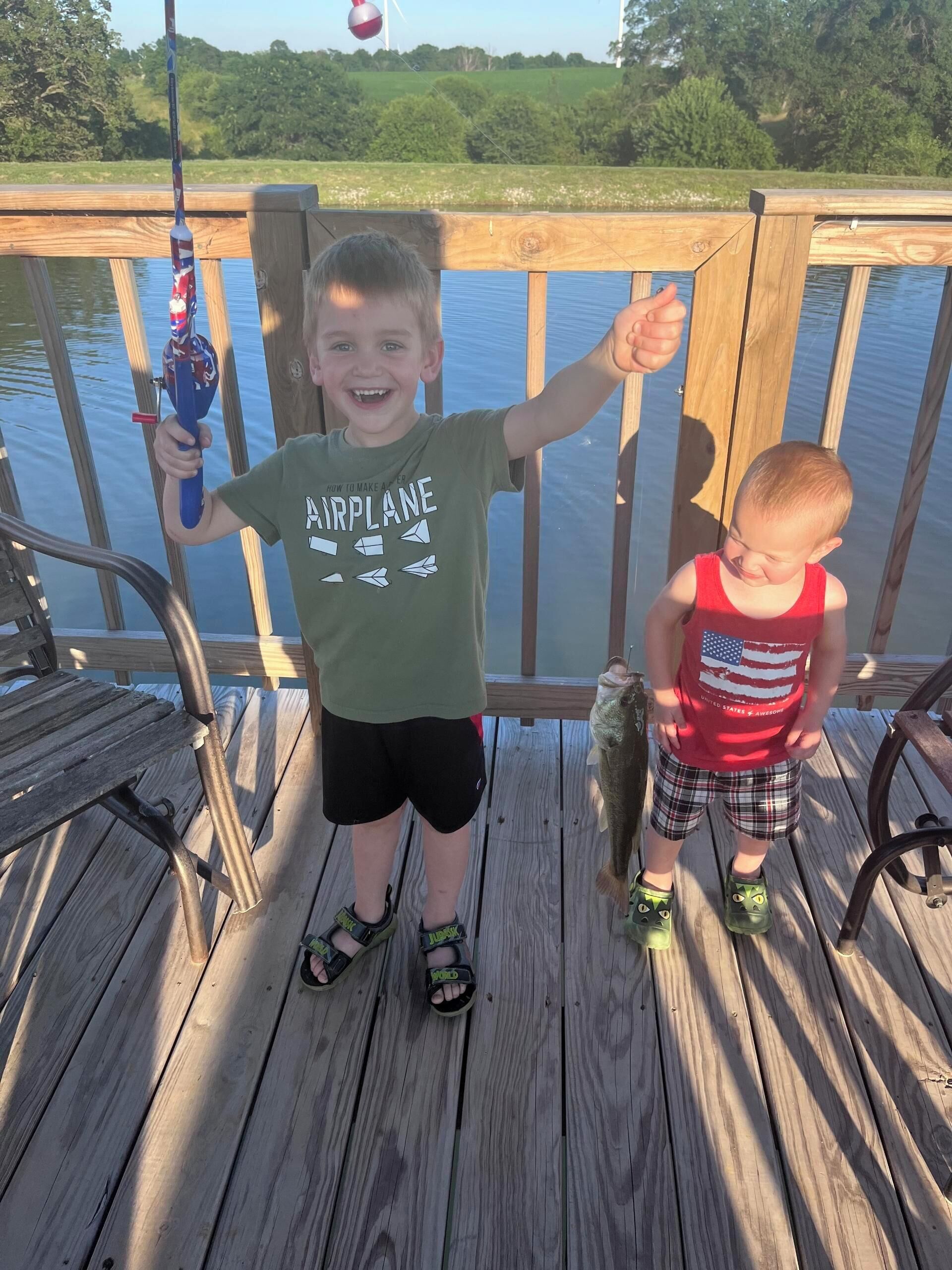 Due bambini su un pontile di legno vicino all'acqua, uno dei quali tiene una canna da pesca.