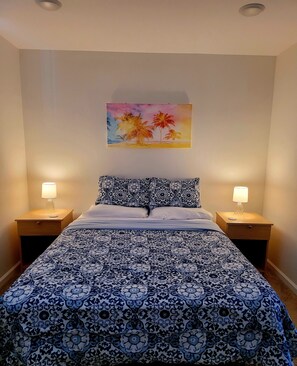 Un dormitorio con una cama, dos mesitas de noche con lámparas, un cuadro colgado en la pared y una colcha estampada.