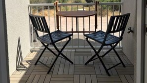 Un terrazzo in legno con due sedie nere e un piccolo tavolo rotondo, con vista su un paesaggio naturale.