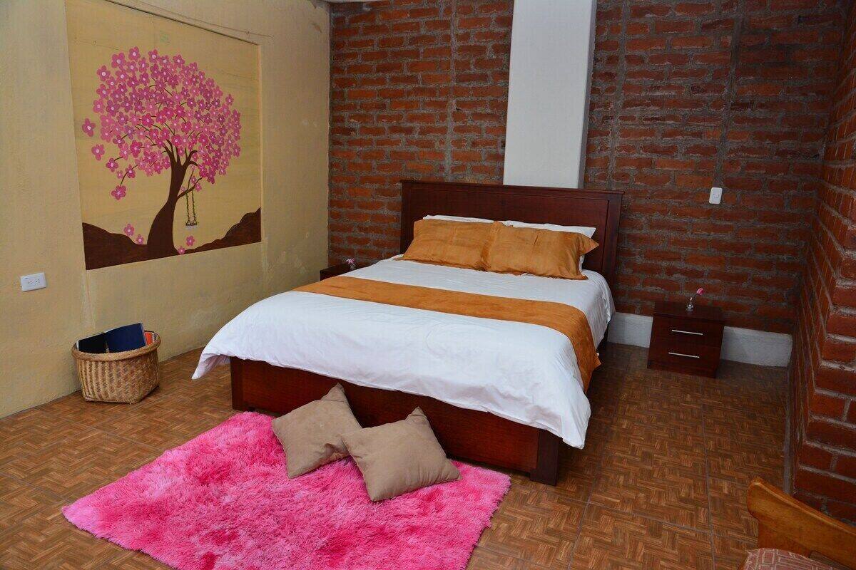 A bedroom with a wooden bed, a pink rug, and a wall painting of a tree.