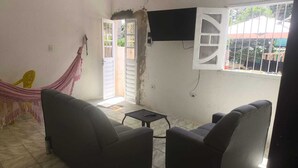 Une pièce comprenant deux canapés, une petite table, un hamac et un téléviseur fixé au mur.