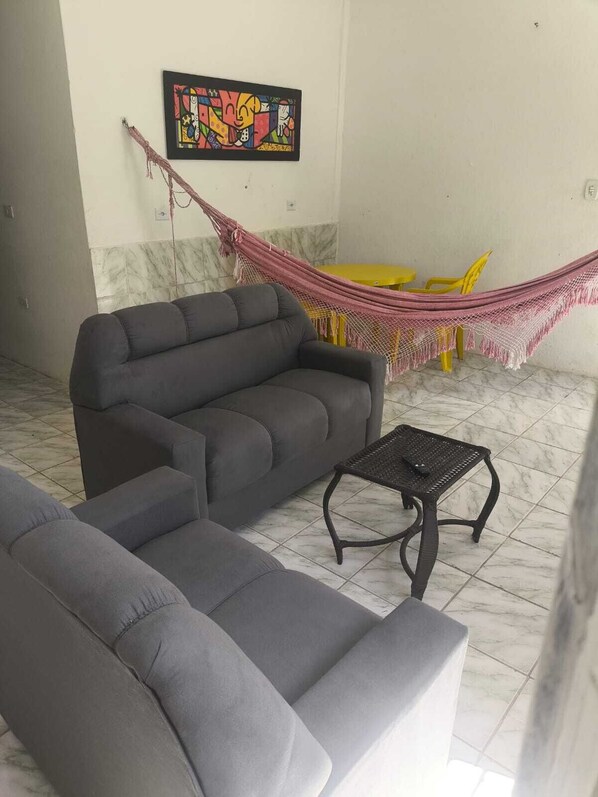 Un salon avec un canapé gris, une petite table noire, un hamac et un tableau coloré accroché au mur.