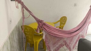 Une pièce avec une table et des chaises jaunes, un hamac et un tableau coloré au mur.