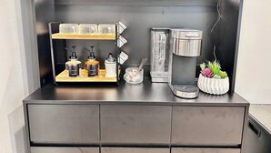 A kitchenette with a coffee maker, a scale, a glass container, and a potted plant. - Studio by the Sound - King Bed • Fire Pit • EV Charger • Pet Friendly (Seattle)