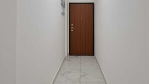 A hallway with a wooden door, white walls, and a marble floor. - Apartmentcomplete with kitchen and personal bathroom located downtown (Bari)