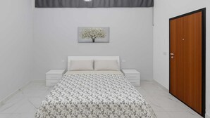 A bedroom with a bed, bedside tables, a wooden door, and a wall-mounted light fixture. - Apartmentcomplete with kitchen and personal bathroom located downtown (Bari)