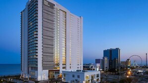 Un grand hôtel moderne, facilement reconnaissable à son enseigne Hilton Grand Vacations, situé près du bord de l’eau et d’une grande roue.