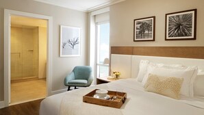 Une chambre d’hôtel avec un lit, une chaise, un plateau avec une tasse et une assiette, et deux tableaux encadrés au mur.