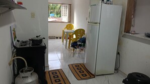 Una cocina pequeña con estufa a gas, un refrigerador y un comedor con sillas amarillas.