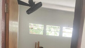 Una habitación pequeña con una cama individual superpuesta, una mesita y un ventilador de techo.