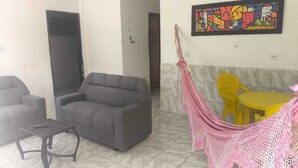 Una sala de estar con un sofá gris, una mesita, una hamaca y una mesa amarilla.