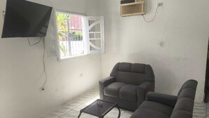Una sala de estar con un sofá, una mesita, un televisor montado en la pared y una ventana con rejas.