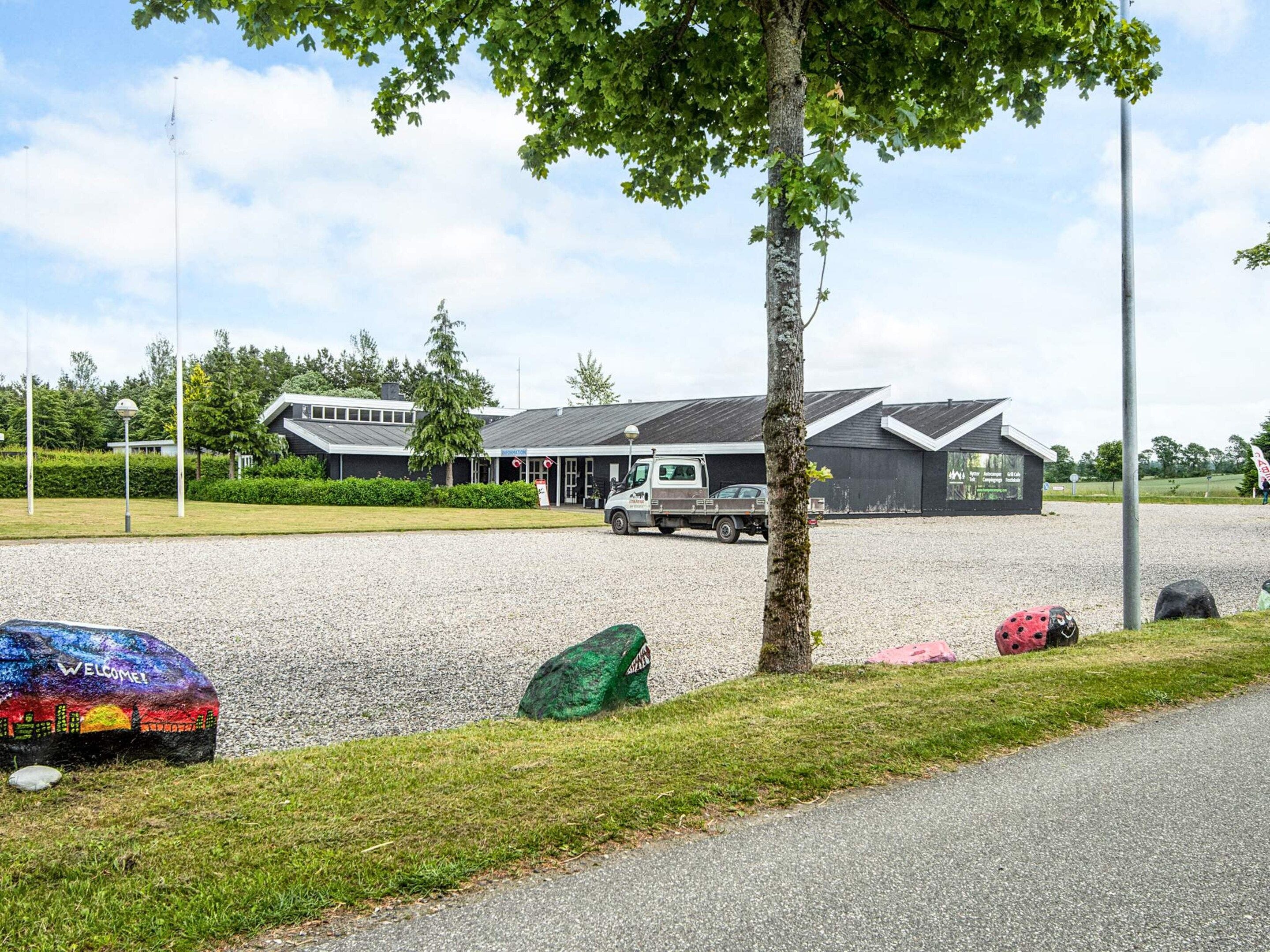 A gravel parking area with a building in the background, a truck, and a tree.