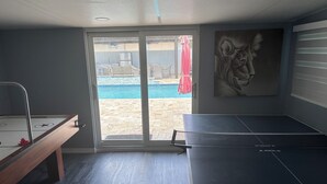 A room with a ping pong table, a small table with a red object, and a sliding glass door leading to a pool area.