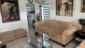 A living room with a beige sofa, a glass coffee table, and artwork on the walls.