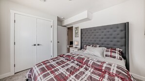 Une chambre à coucher avec un grand lit, une tête de lit rembourrée de couleur grise, une armoire blanche et un luminaire au plafond.