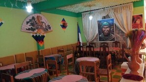 A restaurant with multiple tables and chairs, a flag on the wall, and a portrait. - Olas del titicaca backpackers  (Copacabana)