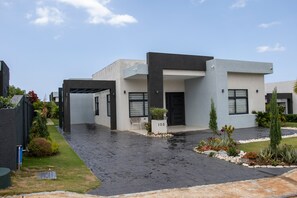 Une maison moderne à deux étages, dotée d’un toit plat, d’une allée couverte et d’un jardin bien entretenu.