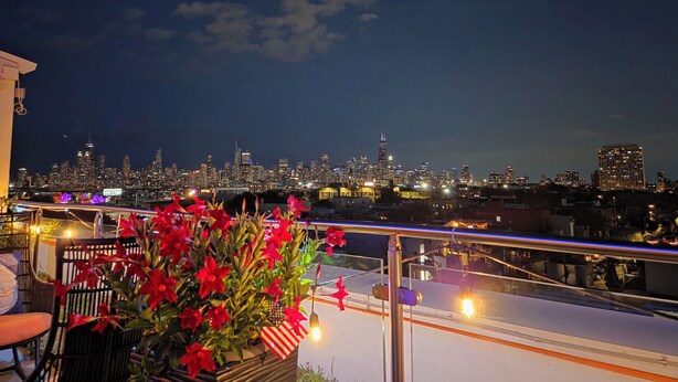 A rooftop terrace with a city skyline view, a potted plant with red flowers, and a chair. - The Beach Loft - 5 min from Whihala Beach, 
 30 min. from Chicago Navy Pier (Whiting)