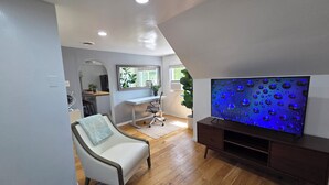 A modern living room with a large flat-screen TV, a white sofa, a wooden floor, and a desk with a computer. - The Beach Loft - 5 min from Whihala Beach, 
 30 min. from Chicago Navy Pier (Whiting)