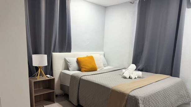 Una habitación de hotel moderna con una cama bien hecha, una lámpara de noche y una mesita de noche de madera.