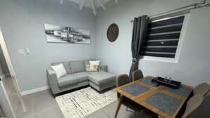Una sala de estar moderna con un sofá modular gris, una mesa de comedor de madera con cuatro sillas, un tapete estampado, un reloj de pared y una ventana con cortinas.