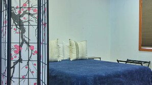 Una habitación con cama, piso de madera, un biombo decorado con flores de cerezo y una ventana con persianas.