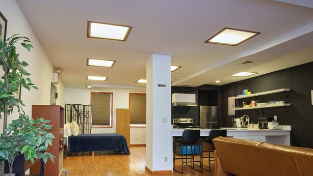 Un interior moderno con piso de madera, una cama, un sofá, una zona de comedor y una cocina.