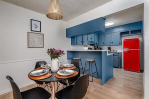 A modern kitchen with blue cabinets, a red refrigerator, and a dining area with a table set for two.