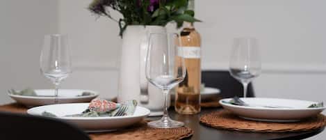 Una mesa de comedor con platos, cubiertos y copas de vino, junto con un florero y una botella de vino.